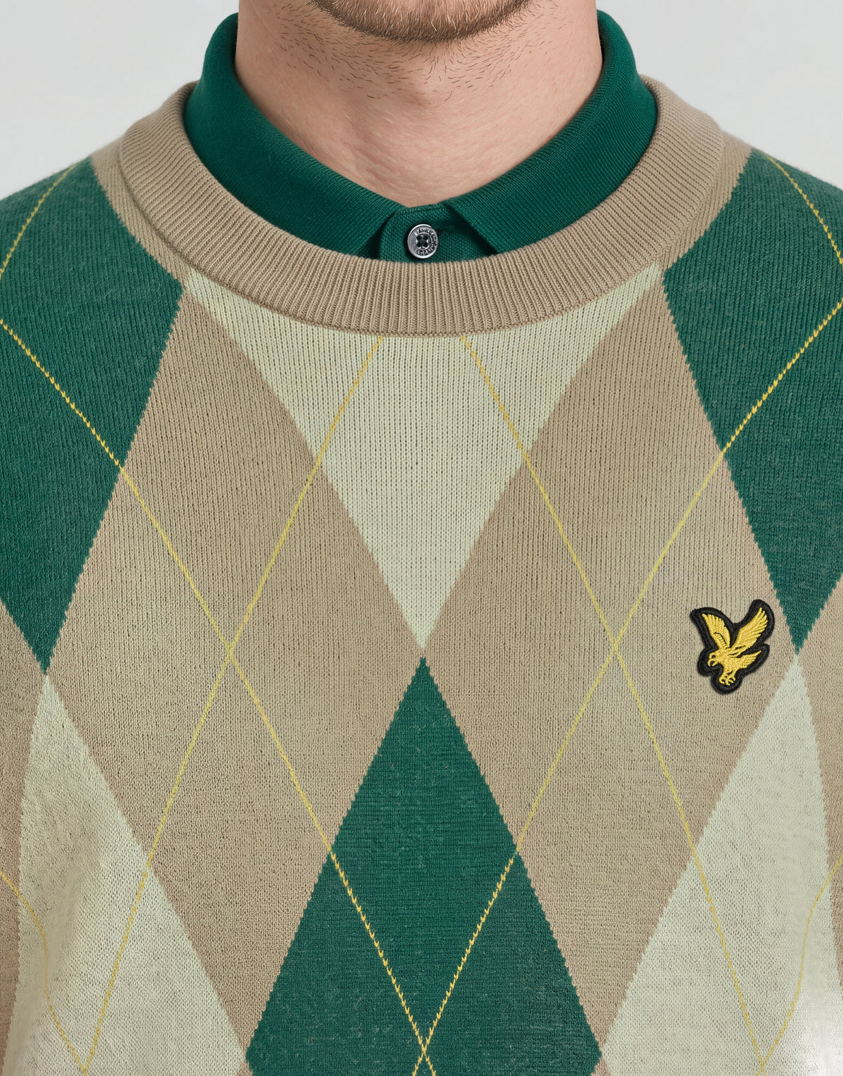 L'uomo indossa un maglione a girocollo con motivo argyle della collezione Archive nei colori cammello e taupe