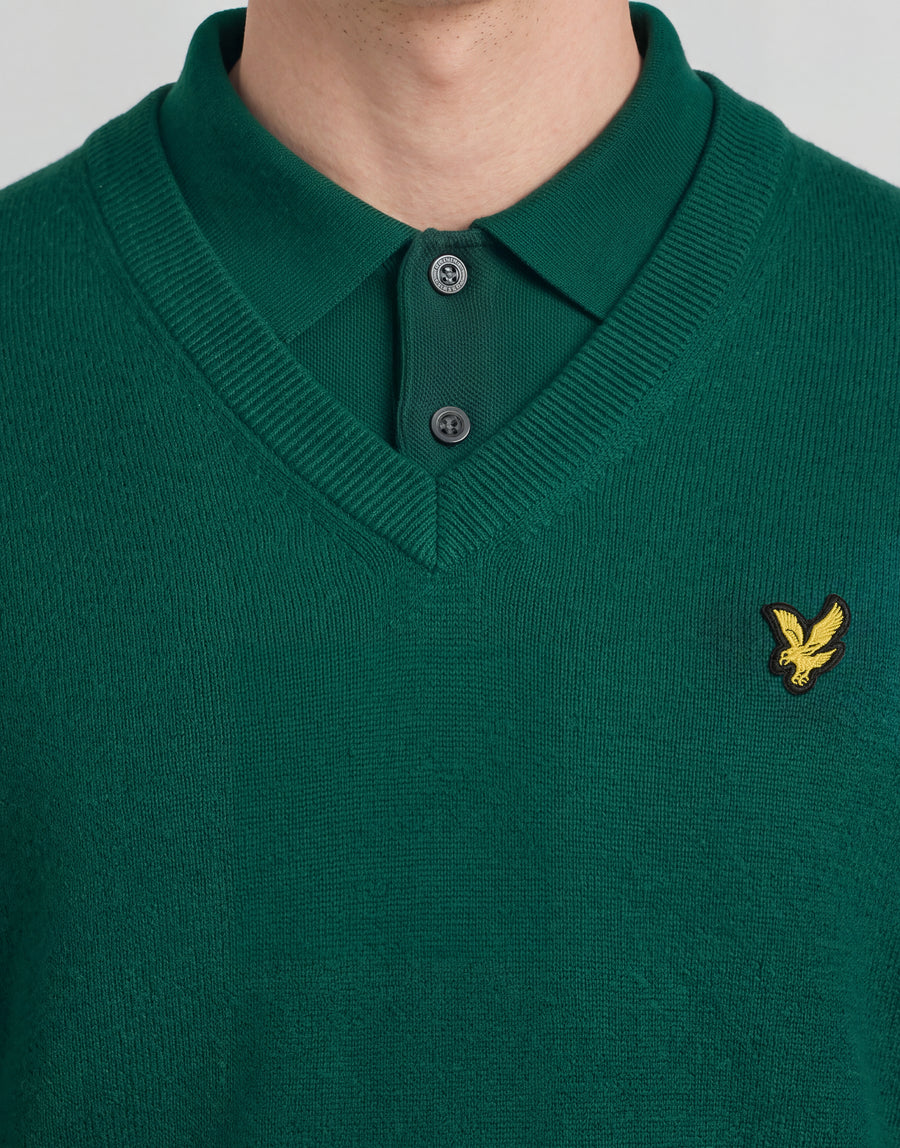 Man draagt een gebreide trui met V-hals uit de Archive-collectie onder een groene jas