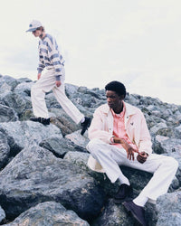 2 men wearing edgy streetwear looks including striped knitwear and a translucent jacket on a rocky landscape