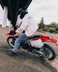Edgy men's outfit featuring an embroidered jacket and on a dirt bike