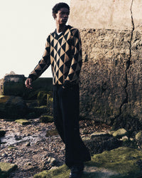Relaxed men's outfit featuring triangle patterned knitwear with logo in a coastal location