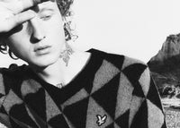 Relaxed men's outfit featuring triangle patterned knitwear with logo in a coastal location