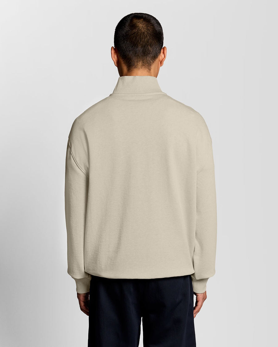 Un homme porte un sweat-shirt à col zippé 1/4 « Heavyweight Script » en coloris « Ice Cream Marl »