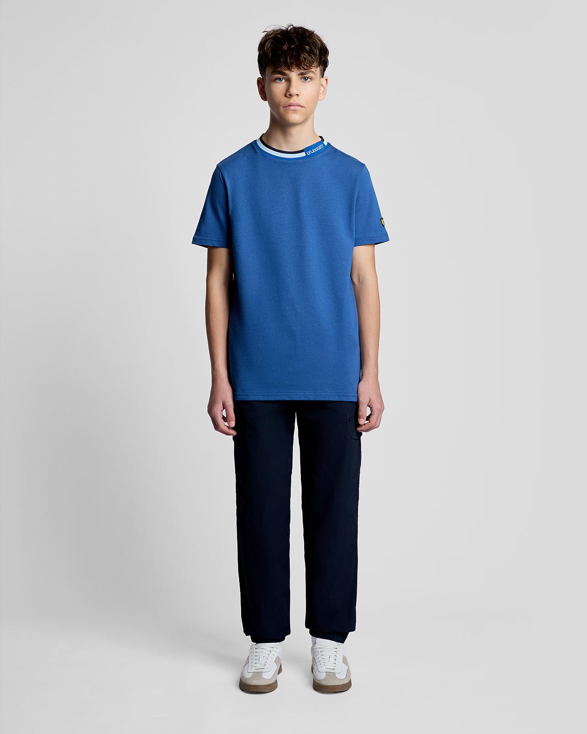 Un homme porte un t-shirt à col rabattu avec logo, couleur bleu barbeau foncé
