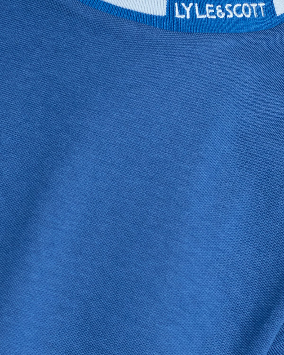 Un homme porte un t-shirt à col rabattu avec logo, couleur bleu barbeau foncé