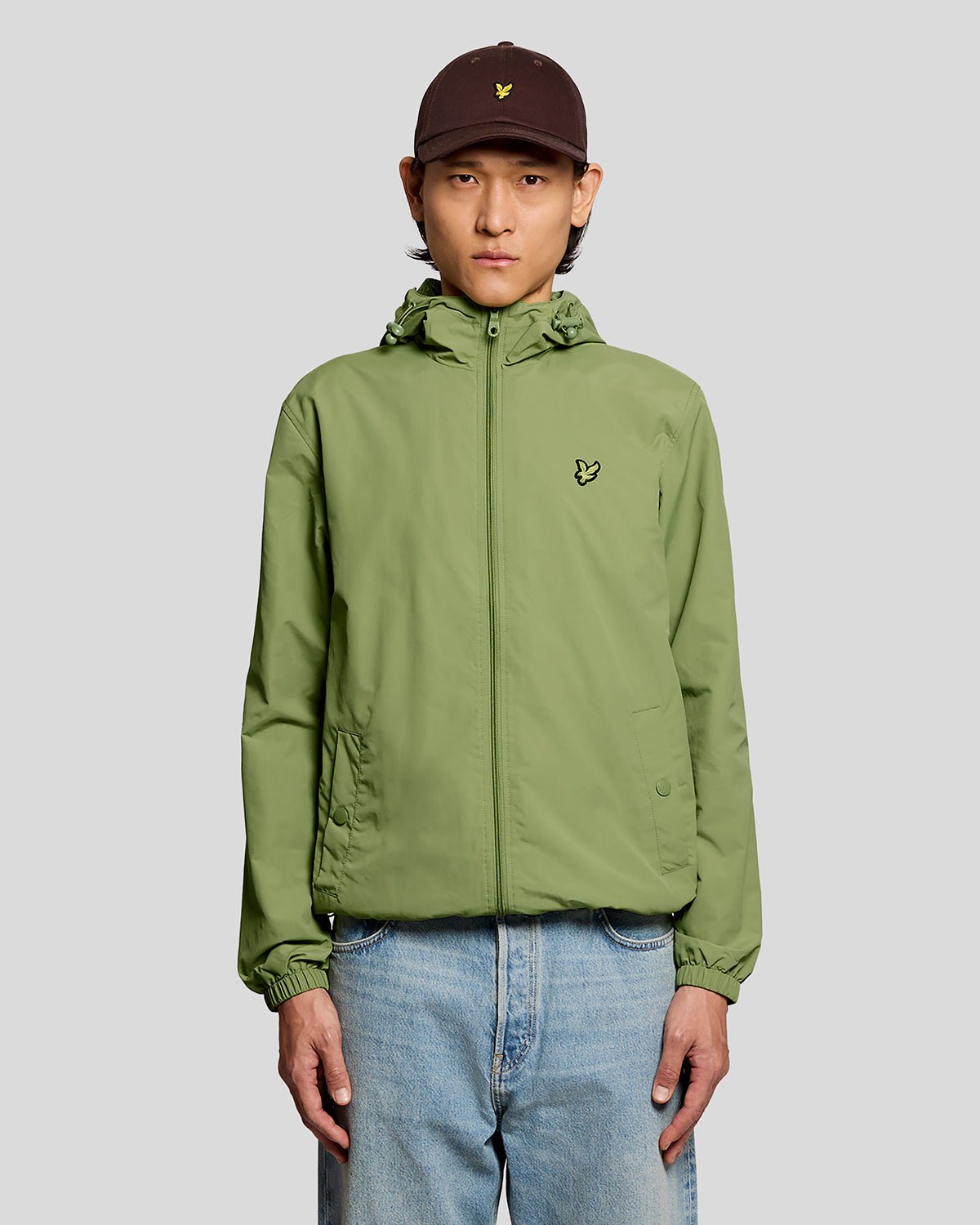 Uomo con giacca con cappuccio resistente all'acqua in verde arbusto