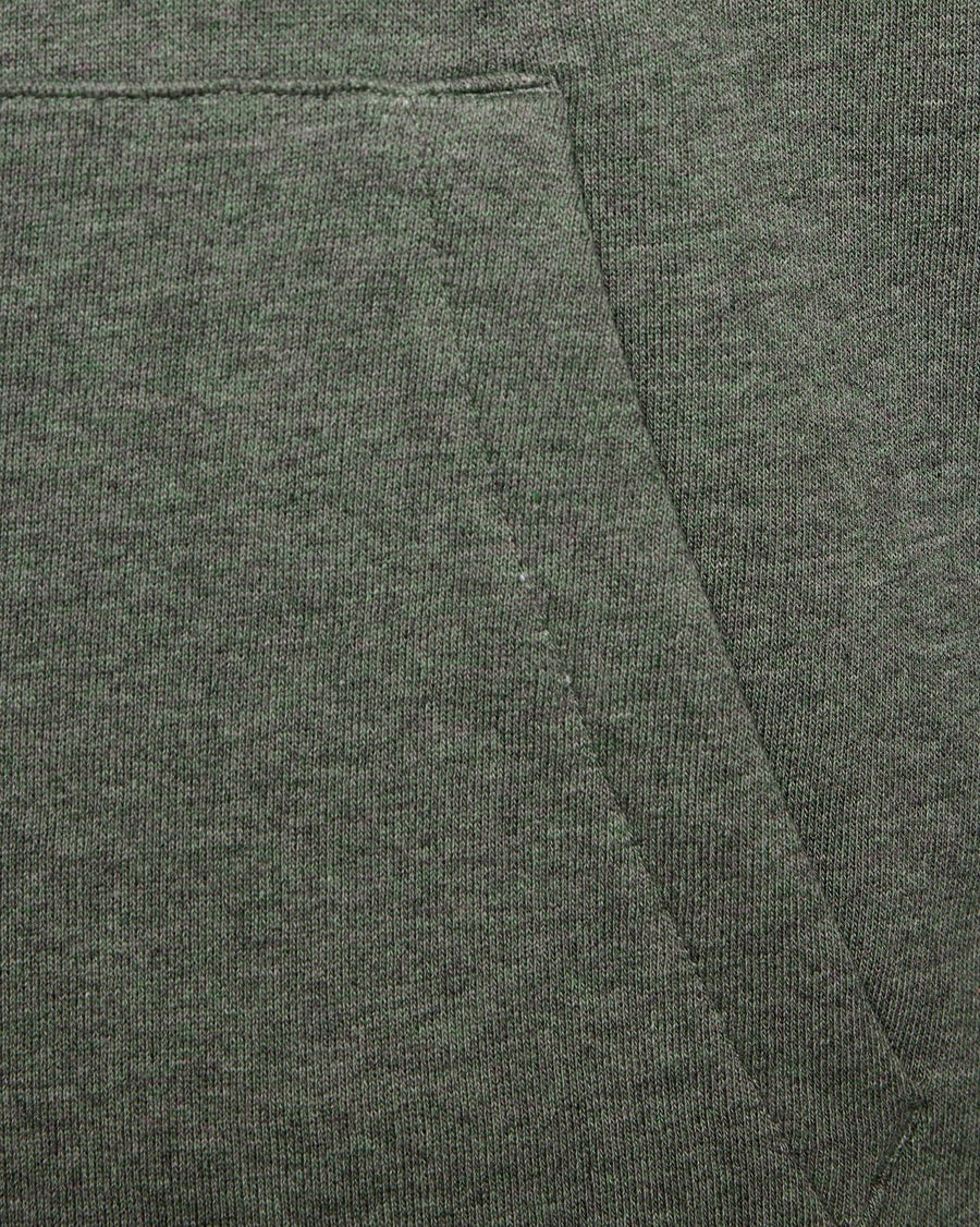 Un homme porte un sweat à capuche raglan en coton chiné, couleur kaki tricolore