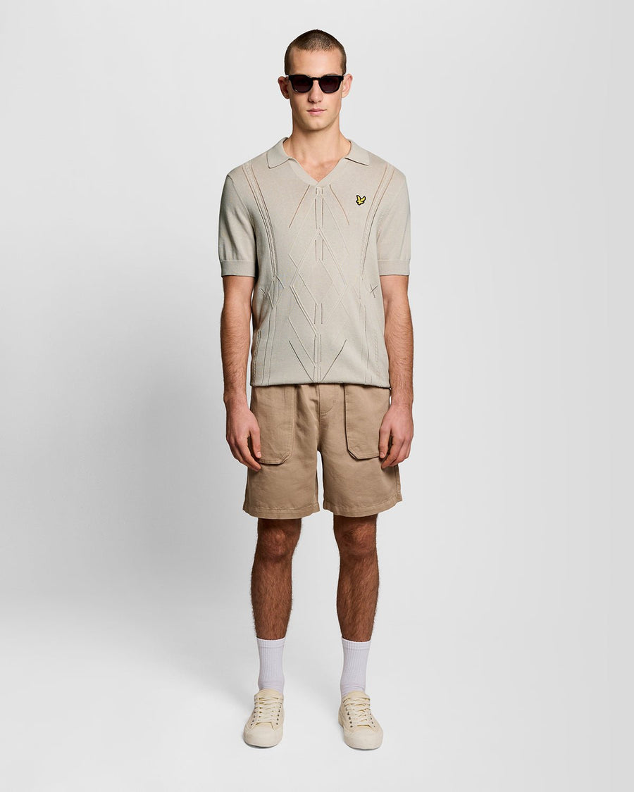 Un homme porte un polo en maille à motif argyle et col ouvert, couleur Cove