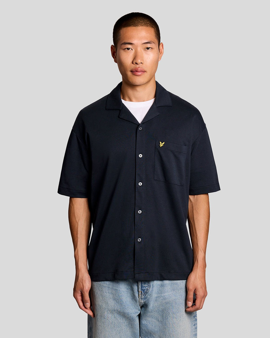 Un homme porte une chemise à manches courtes et col revers, de couleur bleu marine foncé