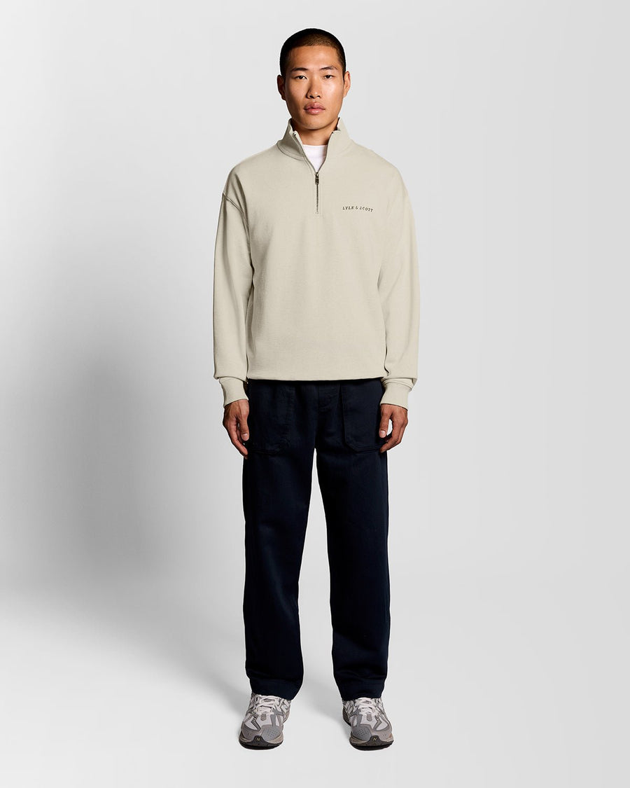 Un homme porte un sweat-shirt à col zippé 1/4 « Heavyweight Script » en coloris « Ice Cream Marl »
