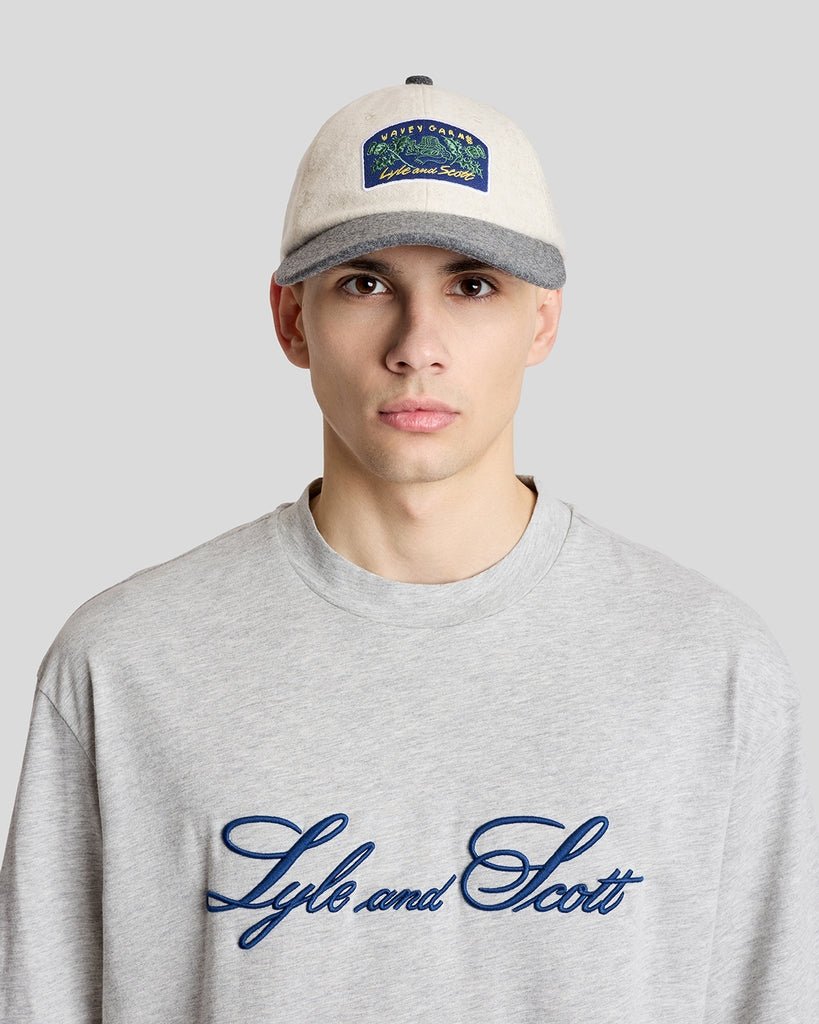 Un homme porte une casquette à patch Wavey Garms de couleur crème