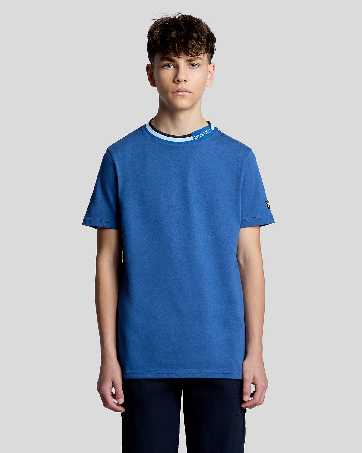 Un homme porte un t-shirt à col rabattu avec logo, couleur bleu barbeau foncé