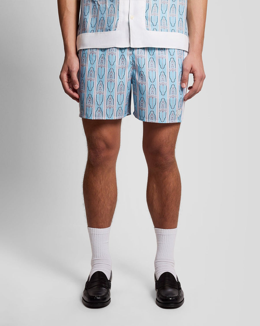 Homme portant un short de bain à motifs floraux, couleur crème amande/bleu de Parme