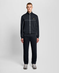 Man wears Straight Leg Piped Track Pants in Dark Navy