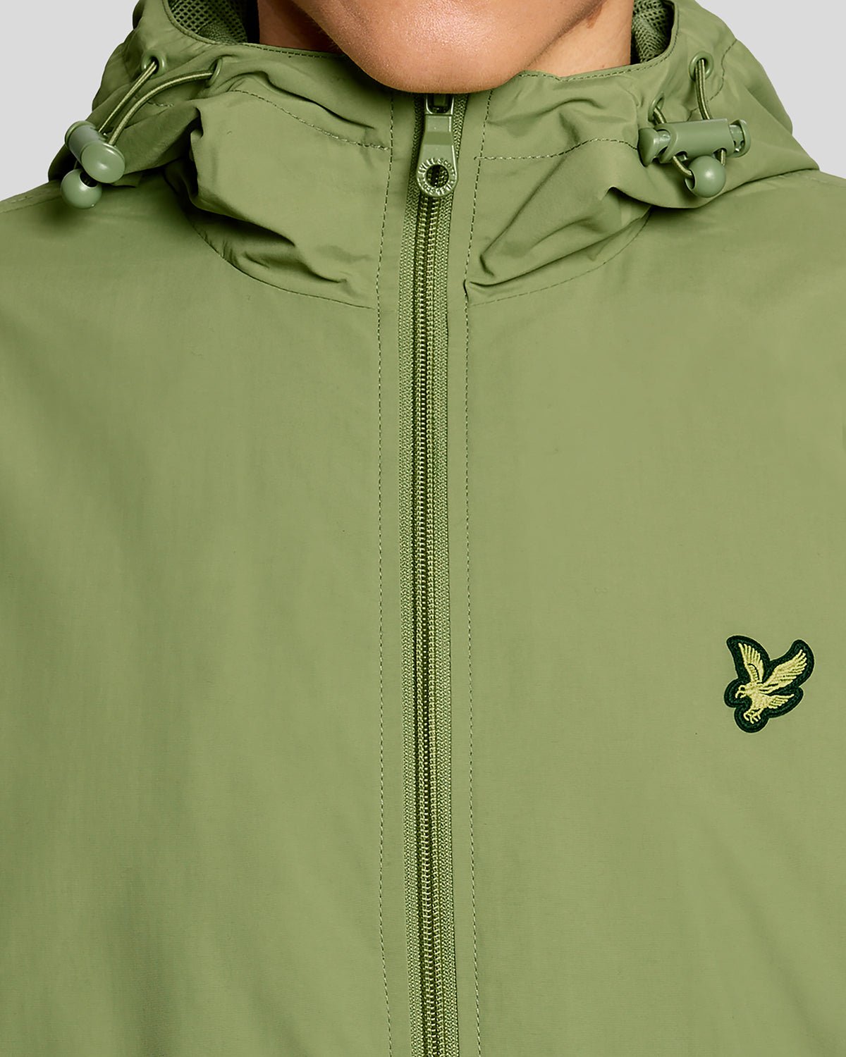 Uomo con giacca con cappuccio resistente all'acqua in verde arbusto