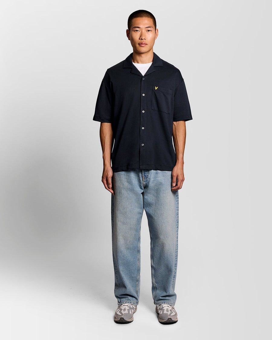 Un homme porte une chemise à manches courtes et col revers, de couleur bleu marine foncé