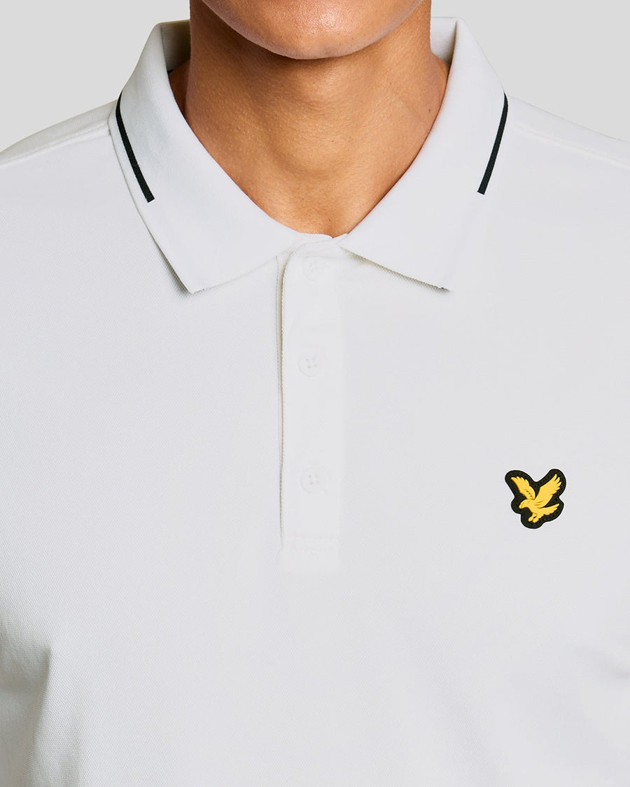 Un homme porte un polo technique à bordures contrastées, de couleur blanche