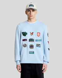 Man wears Wavey Garms Patch Jumper in Home Blue