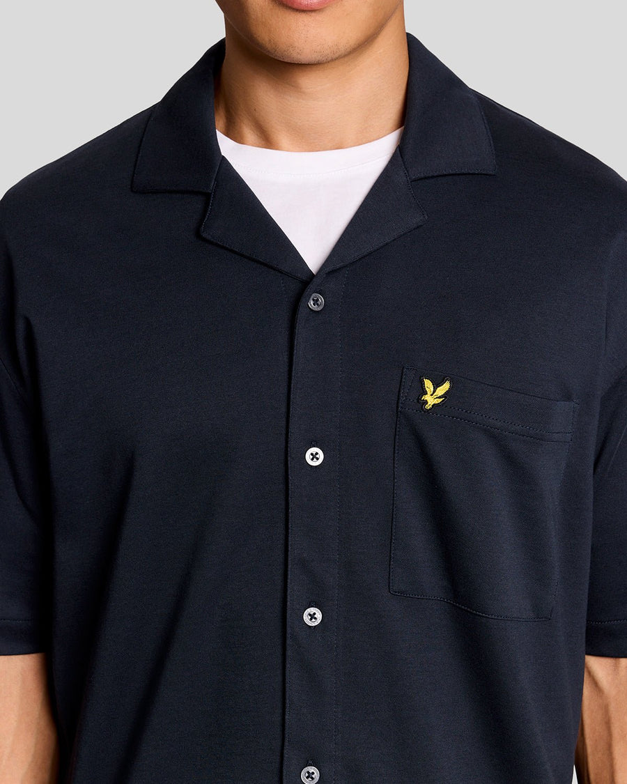 Un homme porte une chemise à manches courtes et col revers, de couleur bleu marine foncé