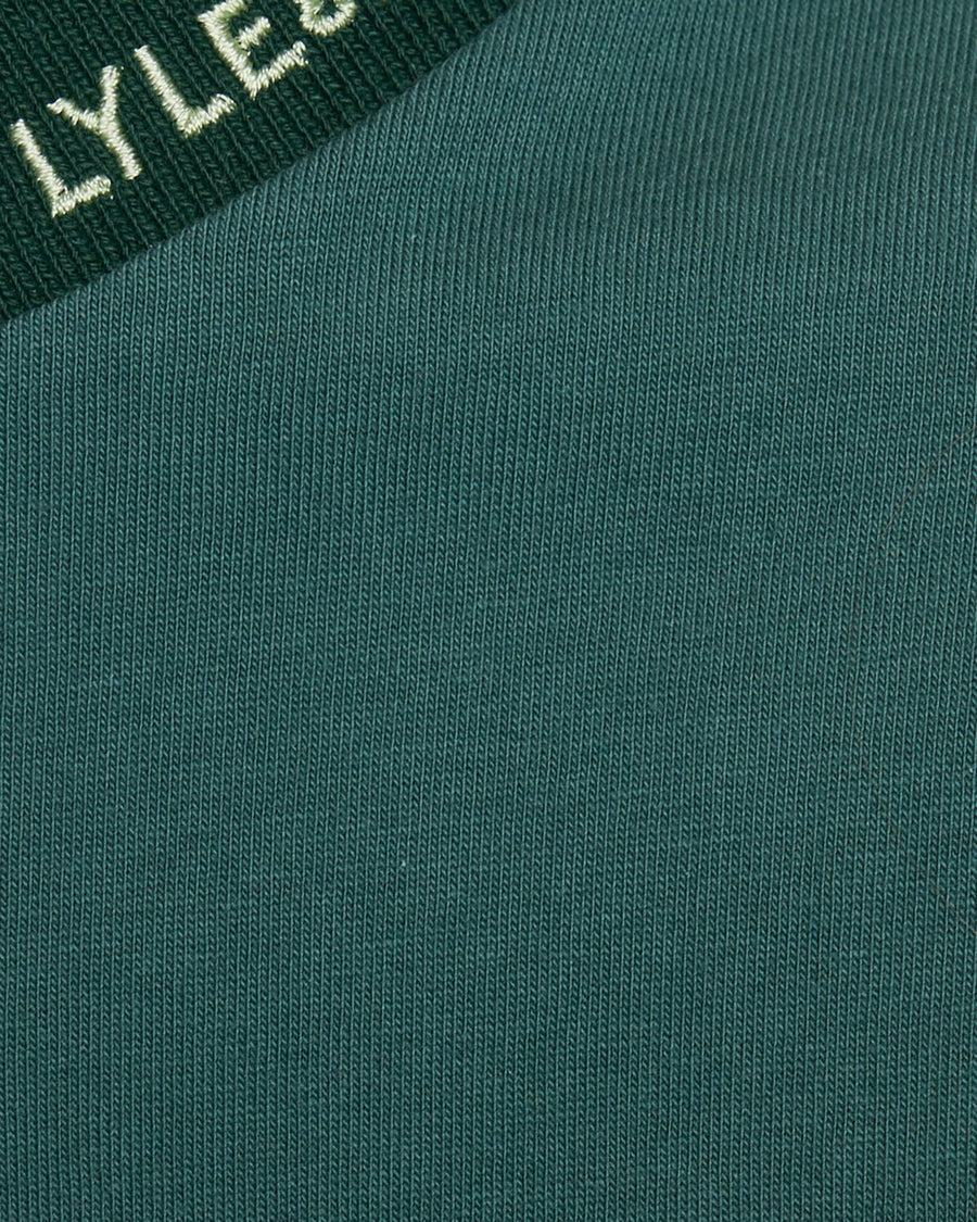 Un homme porte un t-shirt à col relevé avec logo, couleur Everglade