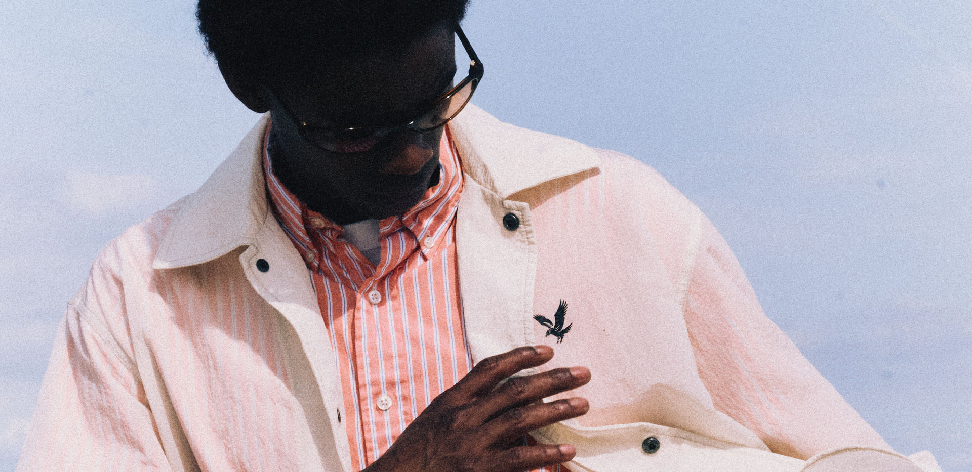 Man wearing a translucent jacket with shirt underneath, staring at the black eagle logo under a blue sky