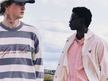 Two men stare into the distance in a rural location, wearing Lyle & Scott knitwear and jackets