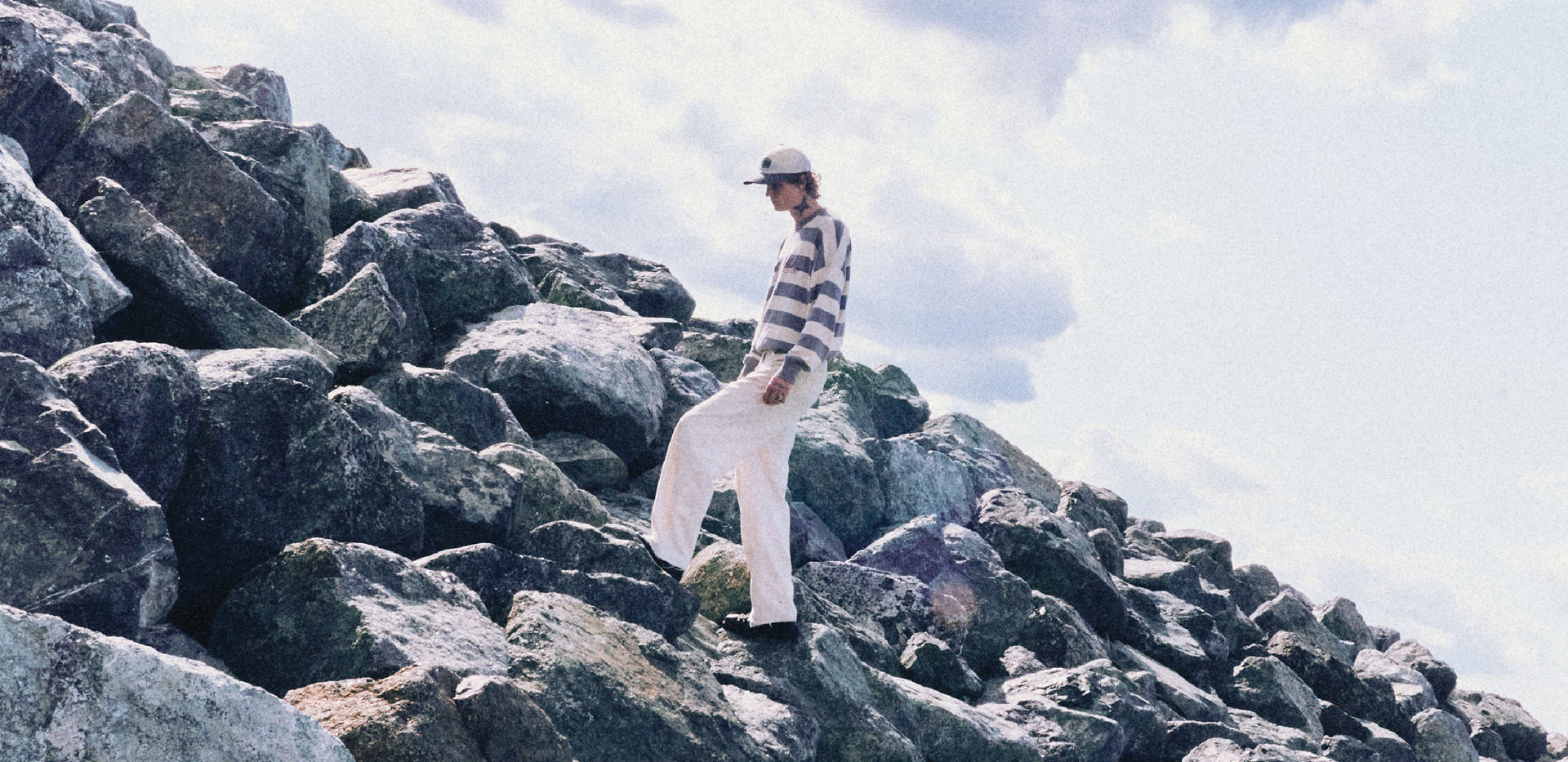 Person standing on rocky terrain with a striped shirt and cap