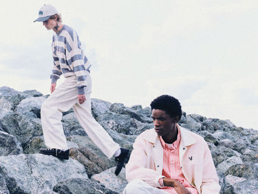 Two people on rocky terrain, wearing a striped jumper and a translucent jacket.