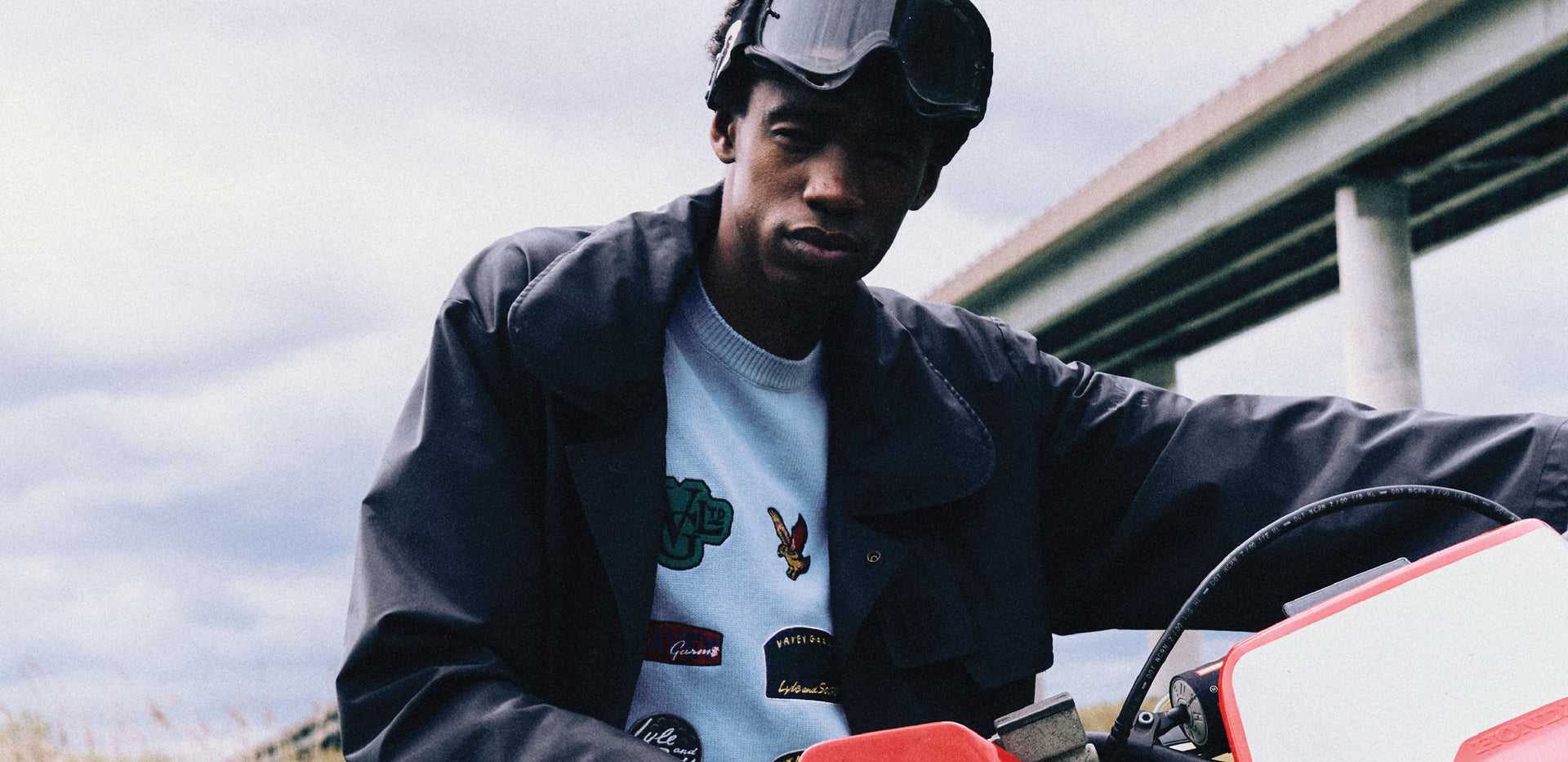 Person wearing a black jacket and blue sweatshirt with embroidered logos, sitting on a motorcycle.